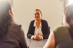 Business employee sitting across from team members at a conference table with hands clasped together