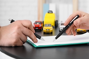Two hands holding pends writing on a piece of paper about auto insurance