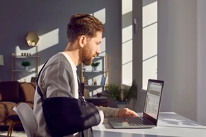 man with broken arm working on laptop computer in office