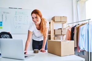 online business owner looking at laptop while preparing deliveries for clients
