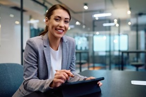 happy female entrepreneur using touchpad while working in office and looking at camera