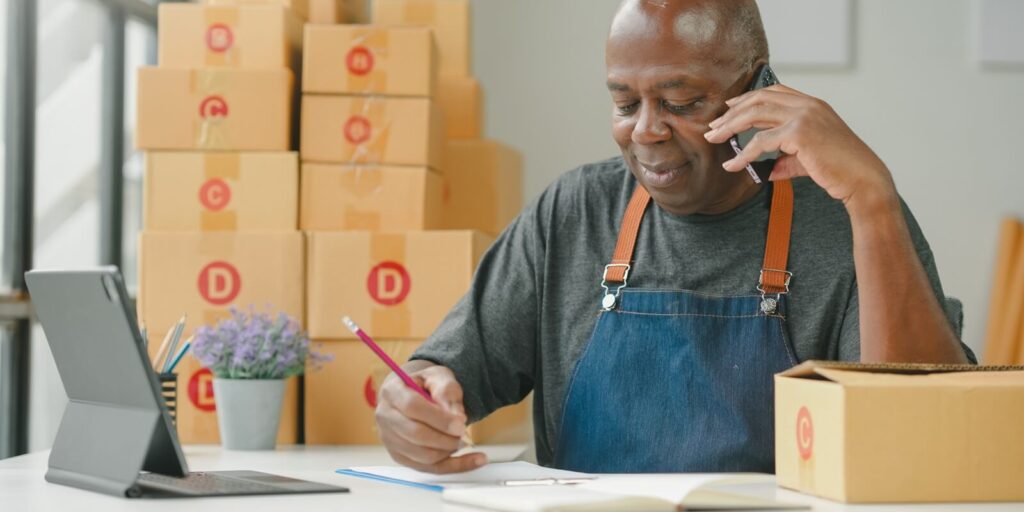 Hawaii small business owner wearing apron at desk with tablet, on phone, writing in notebook