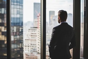 business man in suit in office looking at modern city with skyscrapers through panoramic window