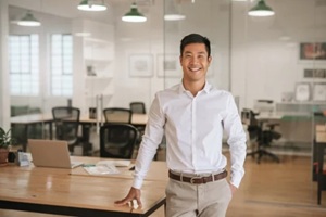young asian businessman standing in an office smiling confidently