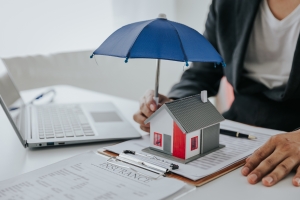 Property Insurance Agent Holding Small Umbrella on Building Miniature Over Documents