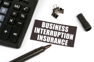 Calculator, Marker and a Black Plate with Text Business Interruption Insurance on Table